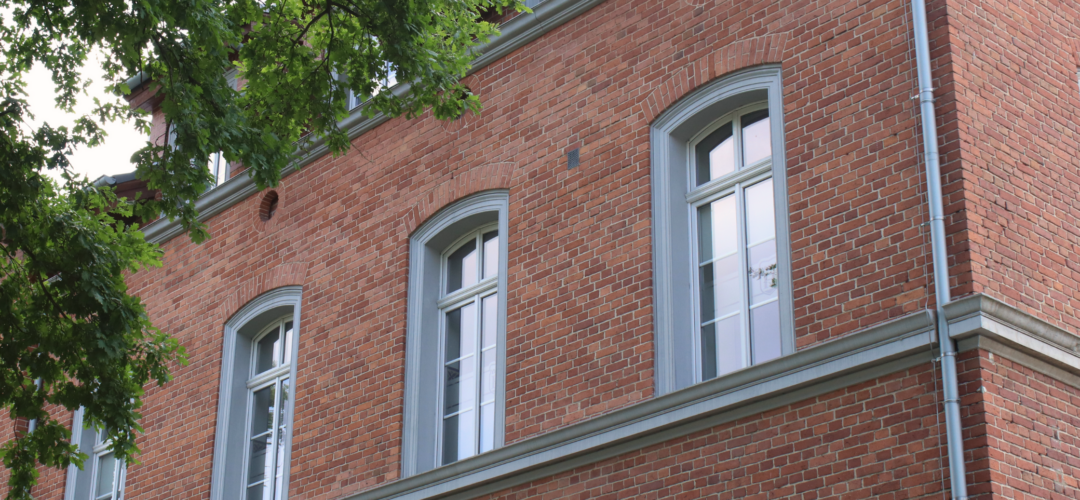Okna ozdobne stylizowane na zabytkowe, które posiadają gzymsy. Stolarka znajduje się na czerwonej, ceglanej fasadzie